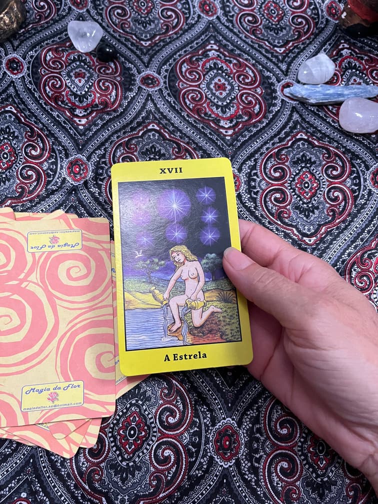 Mão segurando a carta A Estrela sobre a toalha da mesa