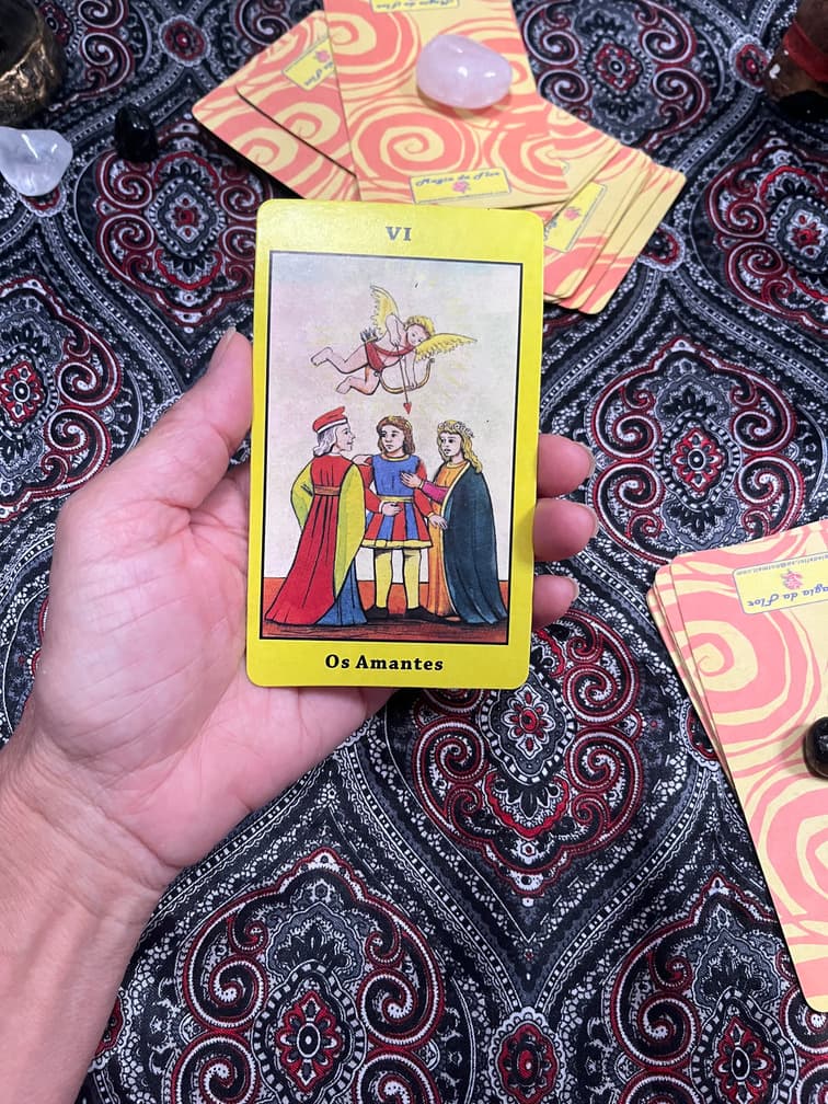 Mão segurando a carta Os Enamorados sobre a toalha da mesa